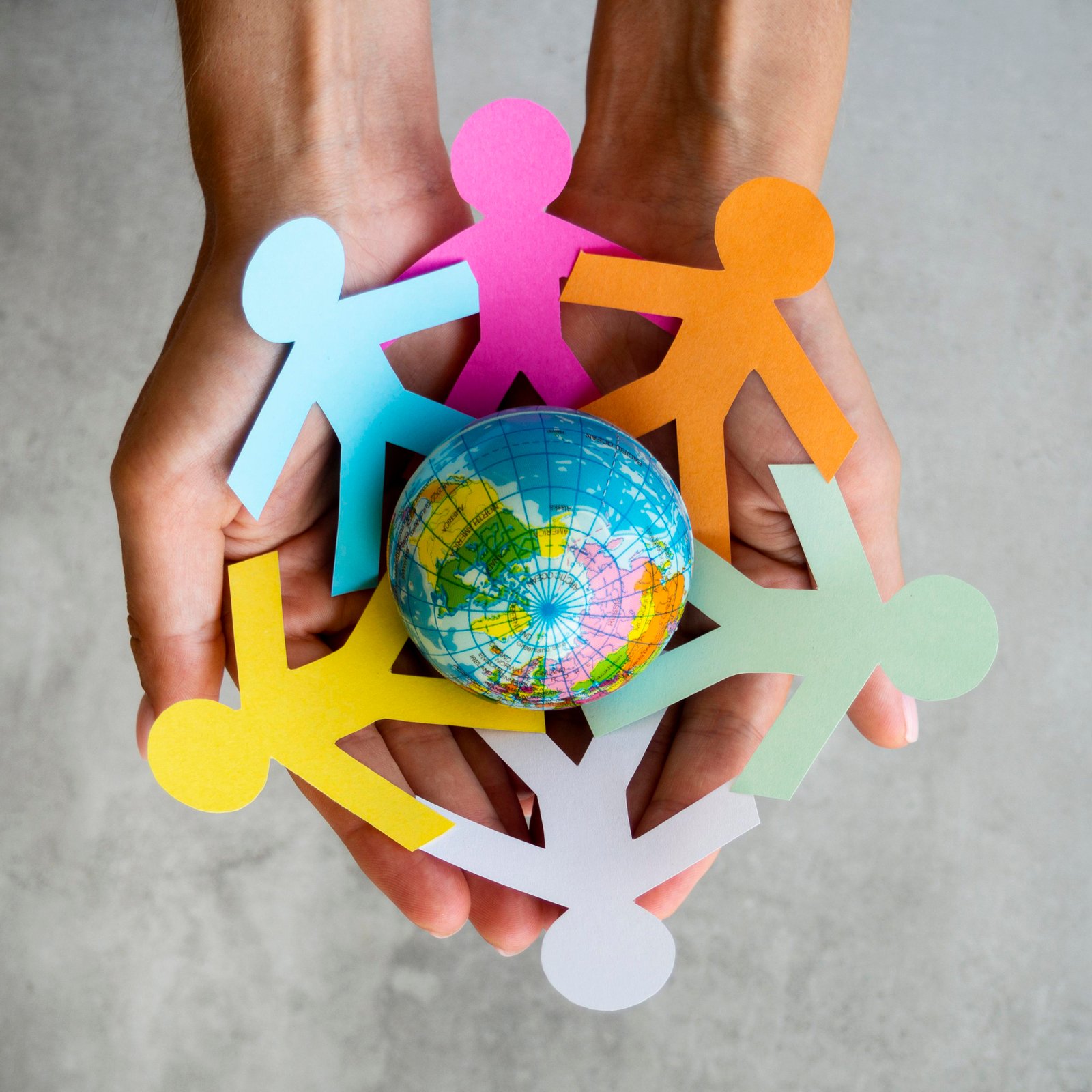 Hands holding a circle of paper figures around a globe